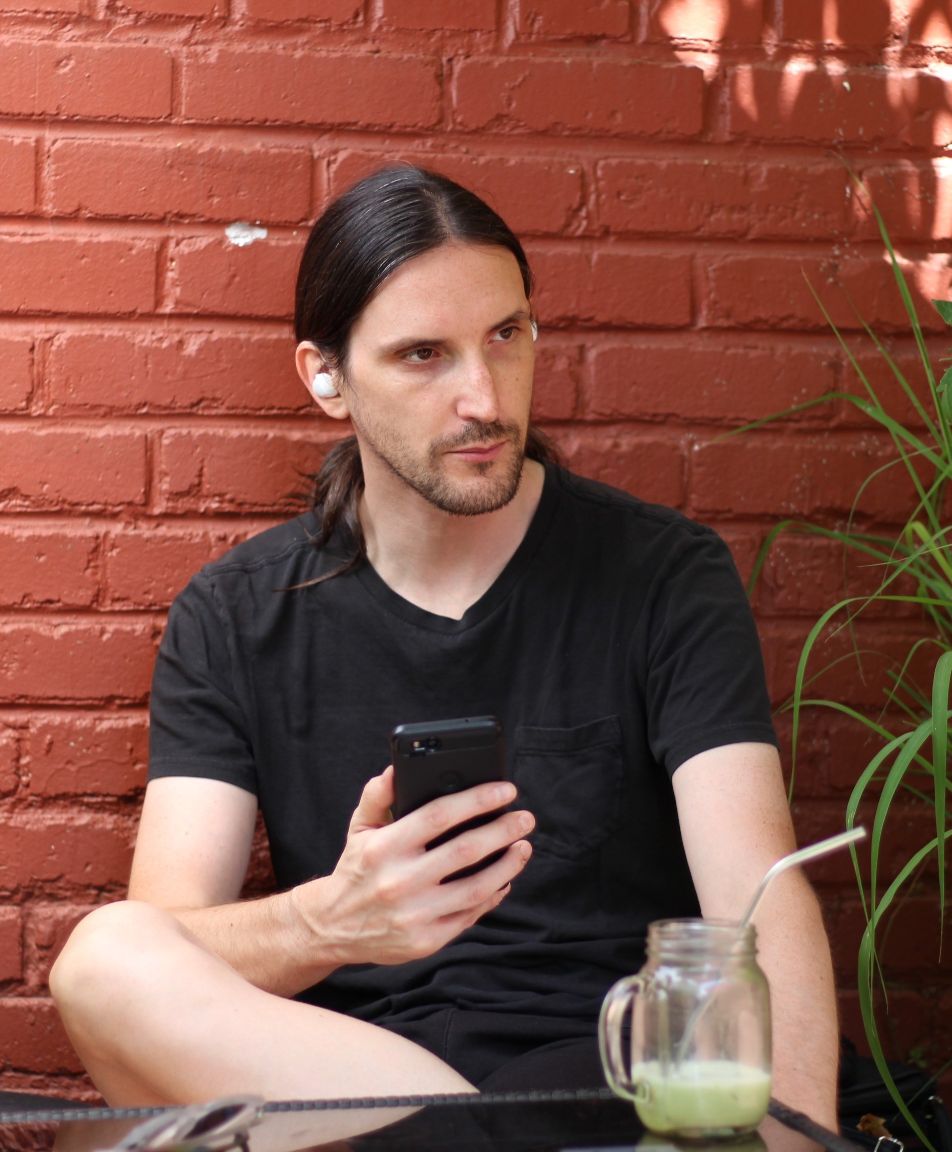 Augustin Delporte GA4 trainer posing with phone in hand, in front of a red brick wall